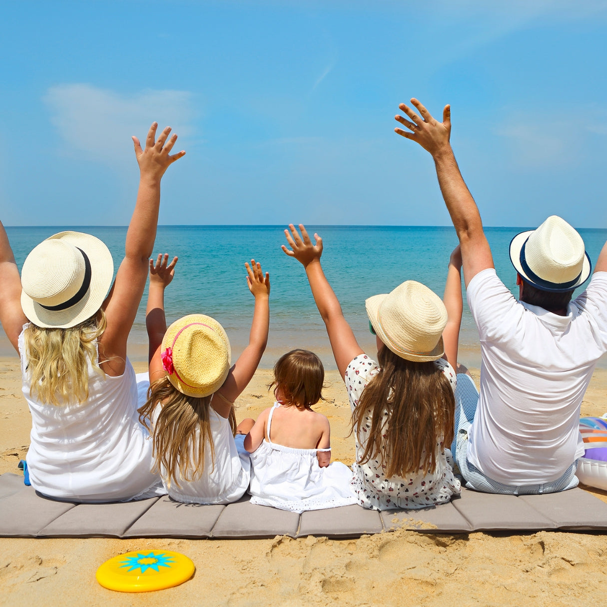 Family of five sitting on a beach with arms raised, enjoying the view.