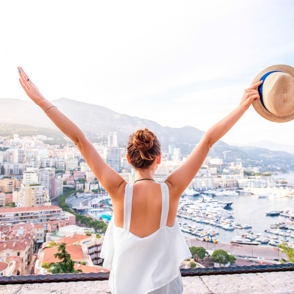 Woman in a white dress with arms raised overlooking a coastal cityscape