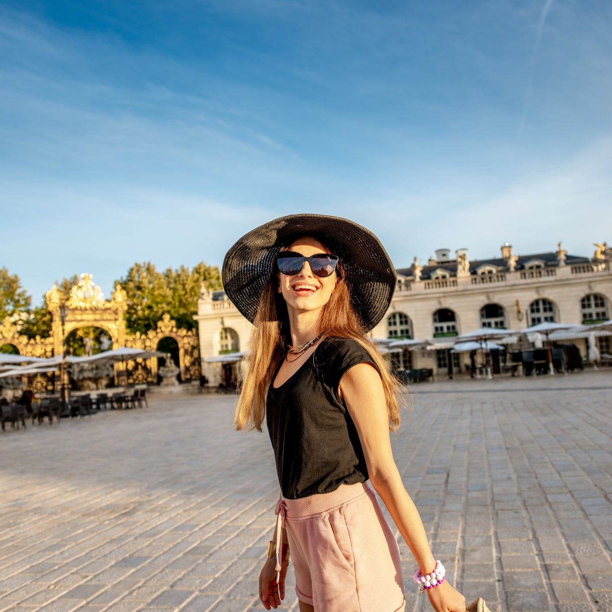 Smiling woman in black sun hat and sunglasses at European plaza
